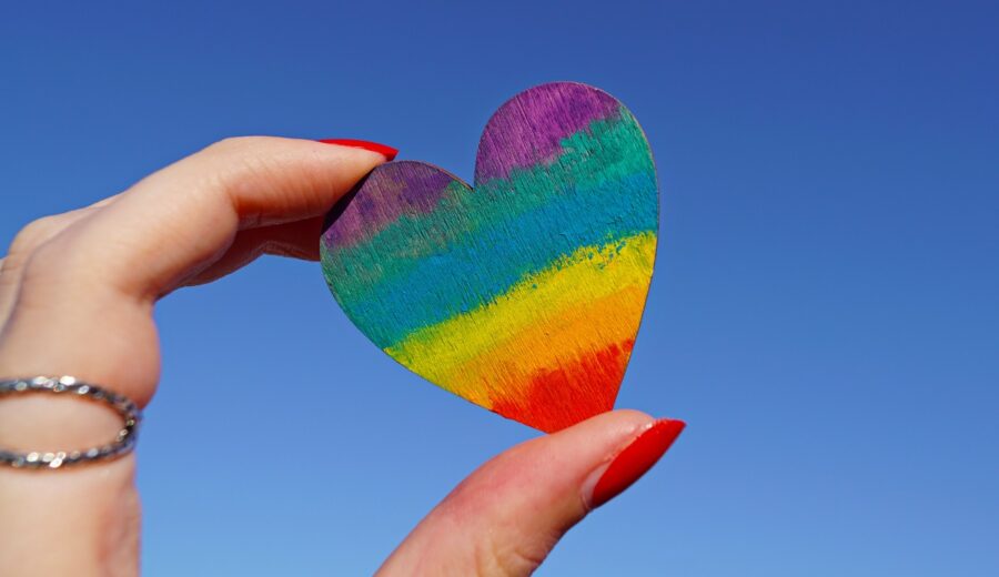 Hand holding up a paper rainbow colored heart to the sky
