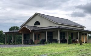 Image of the front of a brown barn with three sided patio on a green field with gray clouds in the sky