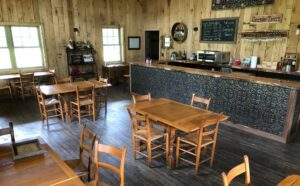 Interior picture of a bar in a room with wooden walls and several wooden tables with four wooden chairs at each